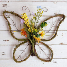 Guirlanda artificial em formato de borboleta com frutinhas em tons pastel e flores para decoração de porta de entrada.