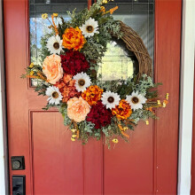 Couronne de fleurs artificielles élégante et imposante, composée de roses rouges, de beige, d'orange et de marguerites. Décoration de porte