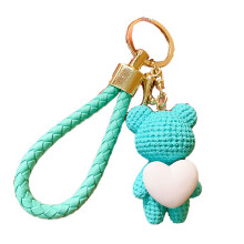 Chaveiro com pingente de urso trançado abraçando um pêssego em forma de coração.