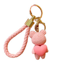 Chaveiro com pingente de urso trançado abraçando um pêssego em forma de coração.