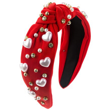 Dameshoofdband met brede rode knoop en hartvormige parel.