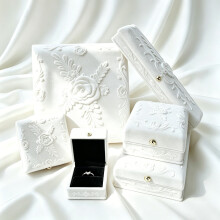 Portagioie bianco con decorazioni in rilievo e rivestimento in tessuto floccato, contenente anelli, bracciali, braccialetti rigidi e ciondoli.
